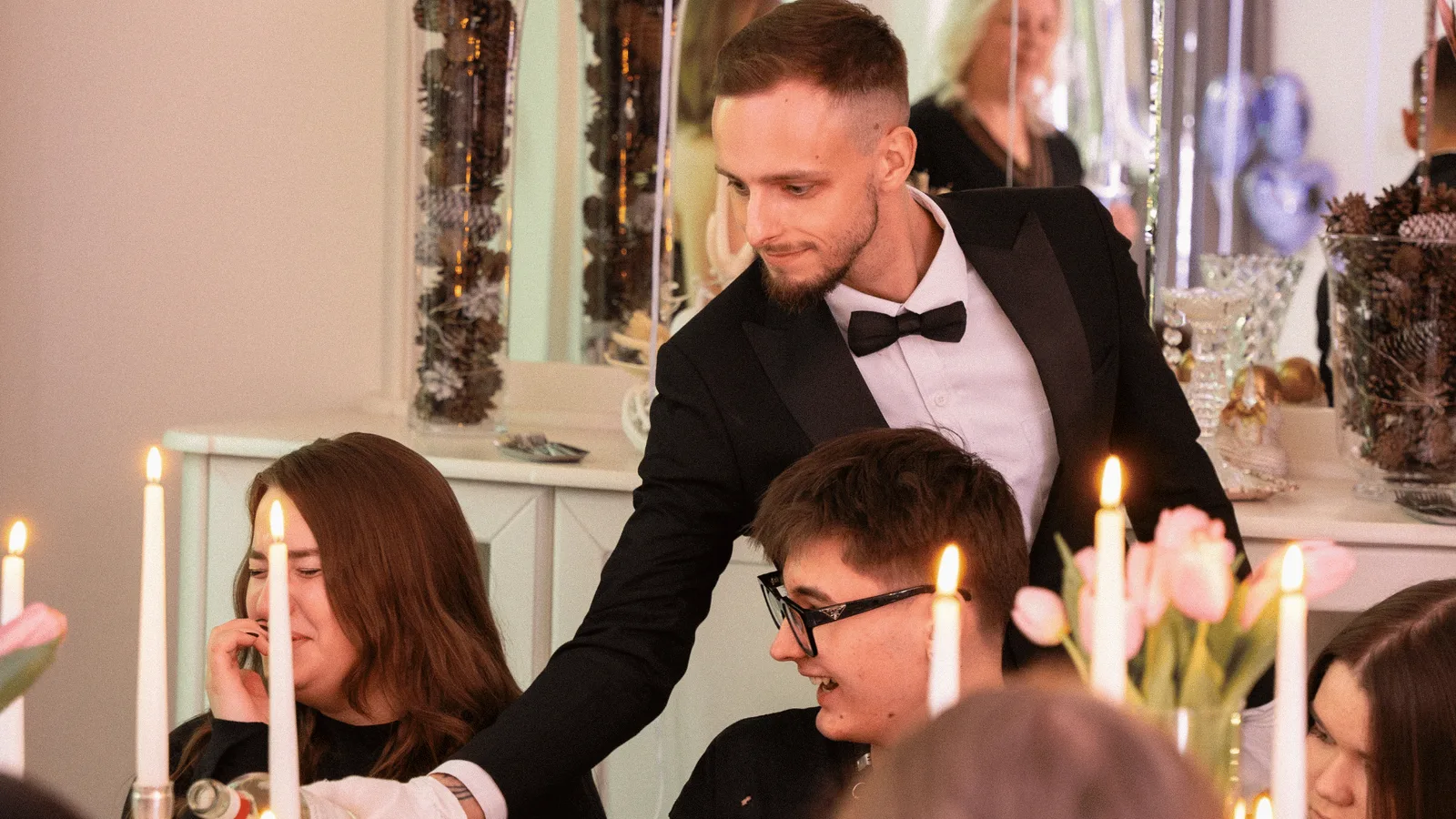 Prowadzący w smokingu wita gości przy świątecznym stole ze świecami na urodzinach
