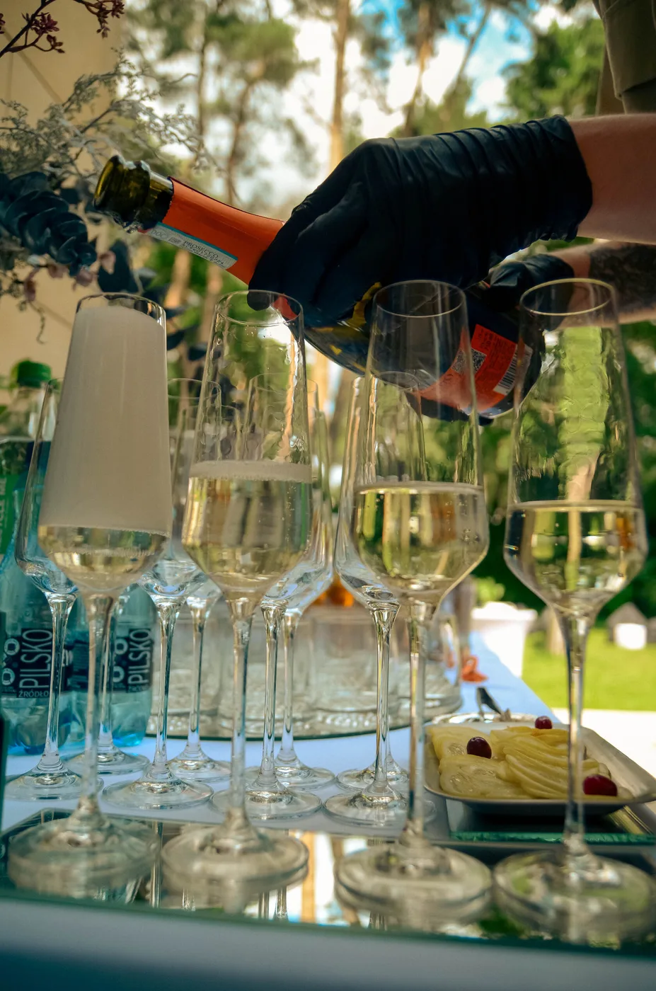 Barman nalewa wino musujące w strefie welcome baru wśród sosnowego lasu