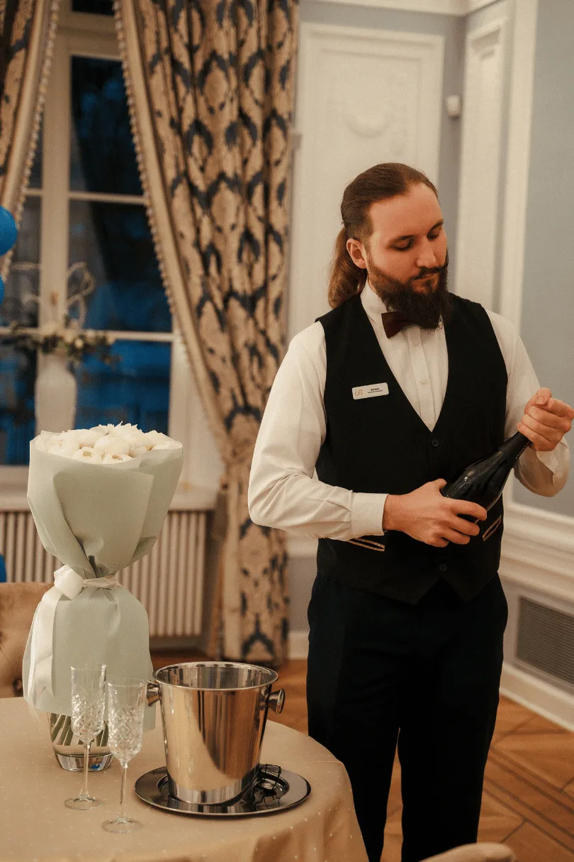 A waiter opening champagne beside a bouquet of white roses at Hotel Bellotto