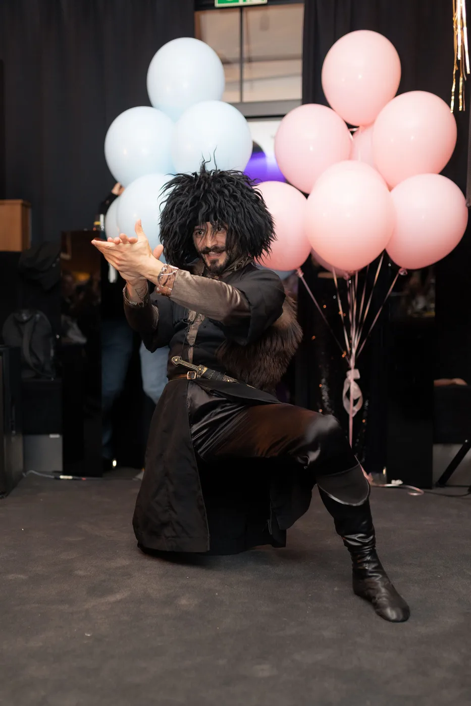 A performer in traditional dress dancing the lezginka beside pink and blue balloons