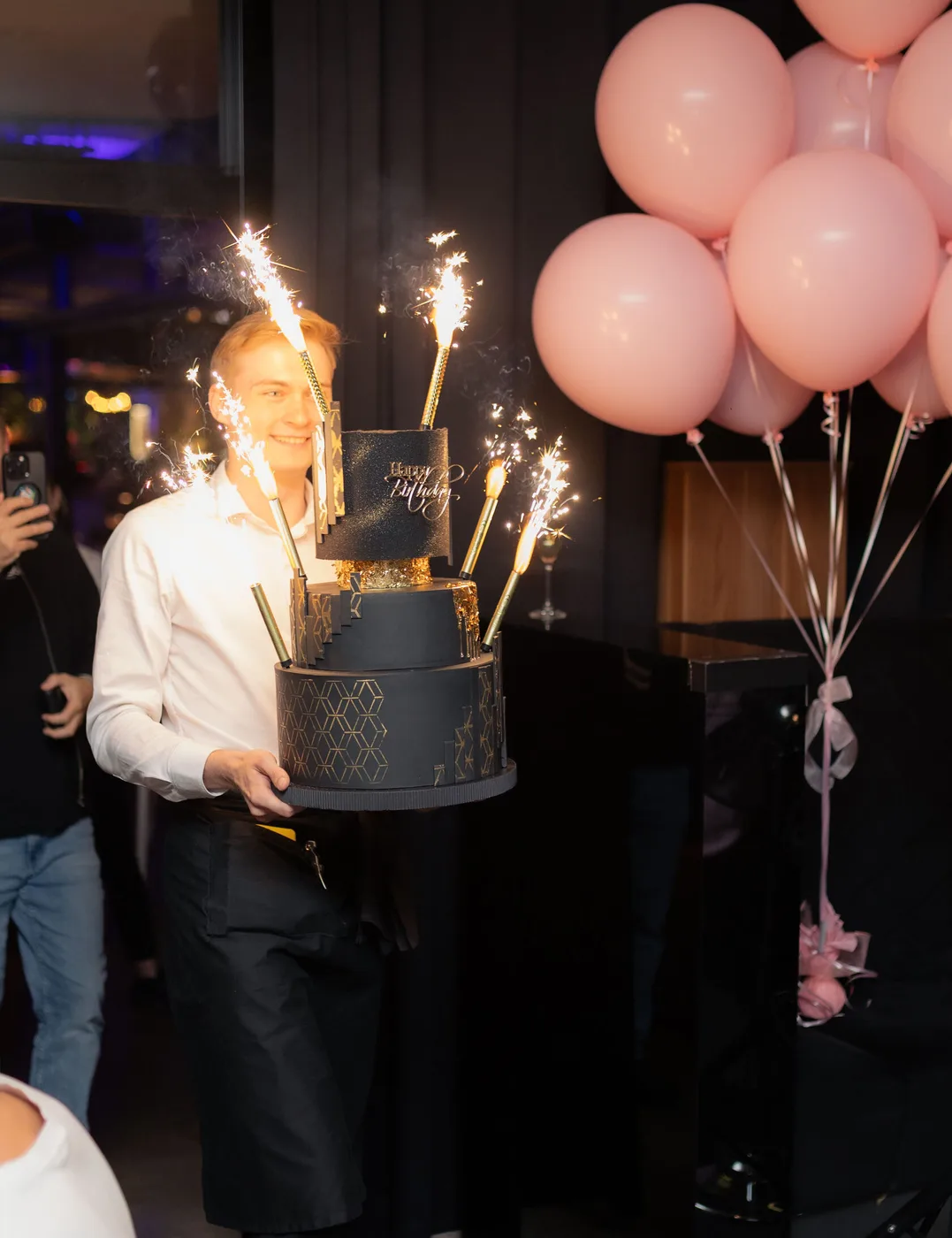 A black-and-gold "Happy Birthday" cake carried out with sparklers