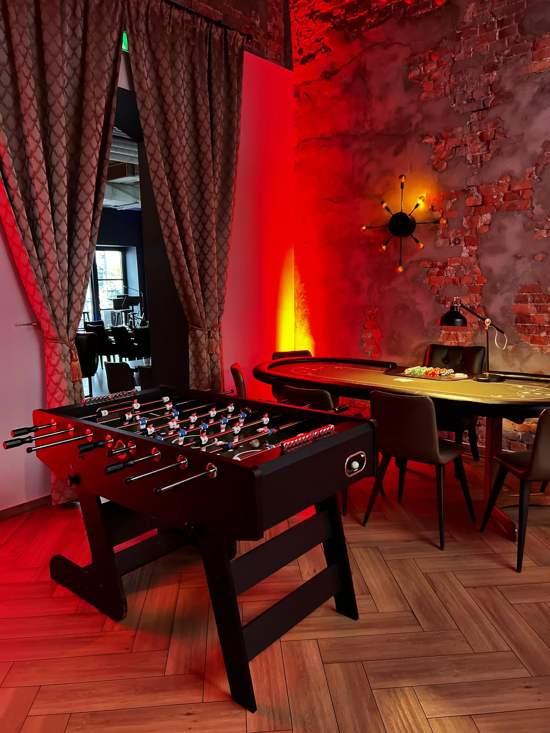 Table football and a poker table with chips in a room with a brick wall and red lighting
