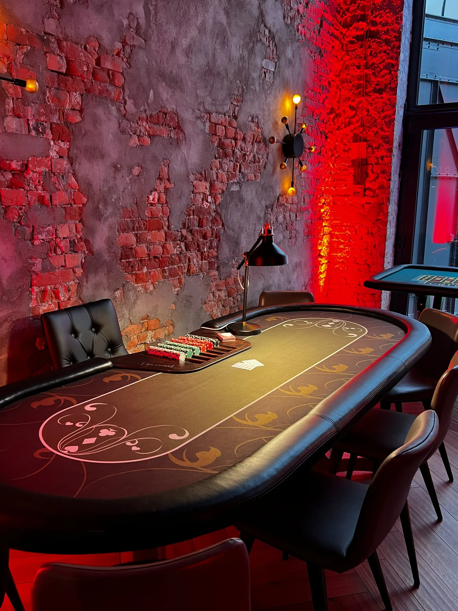Poker table with chips and cards beside a brick wall with red lighting