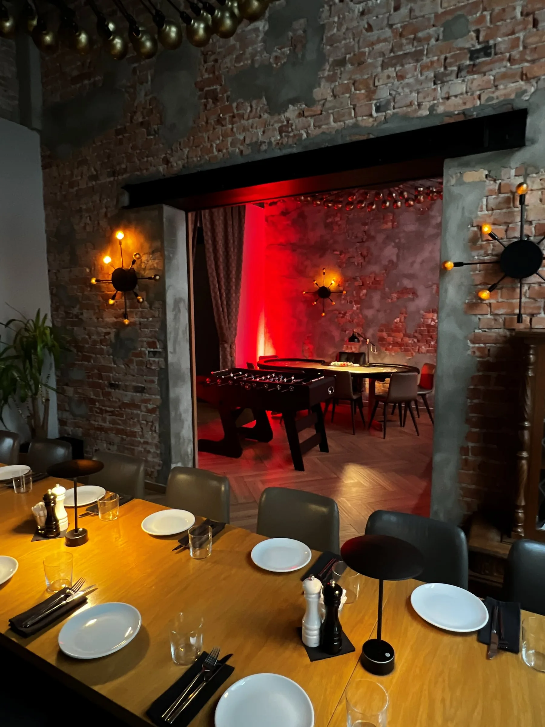 A long set dining table in a restaurant room, with table football and a poker table visible through the doorway