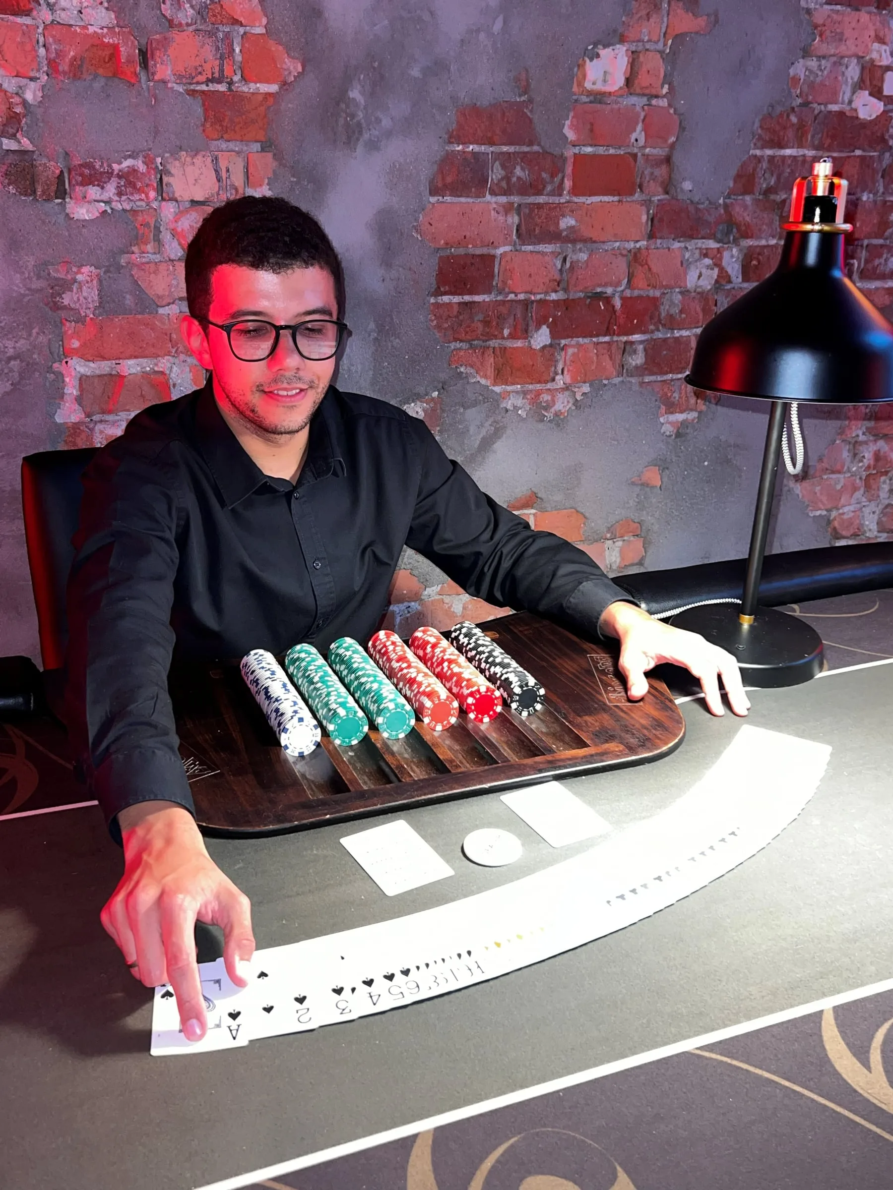 Croupier in a black shirt spreading a deck of cards on a poker table next to chips