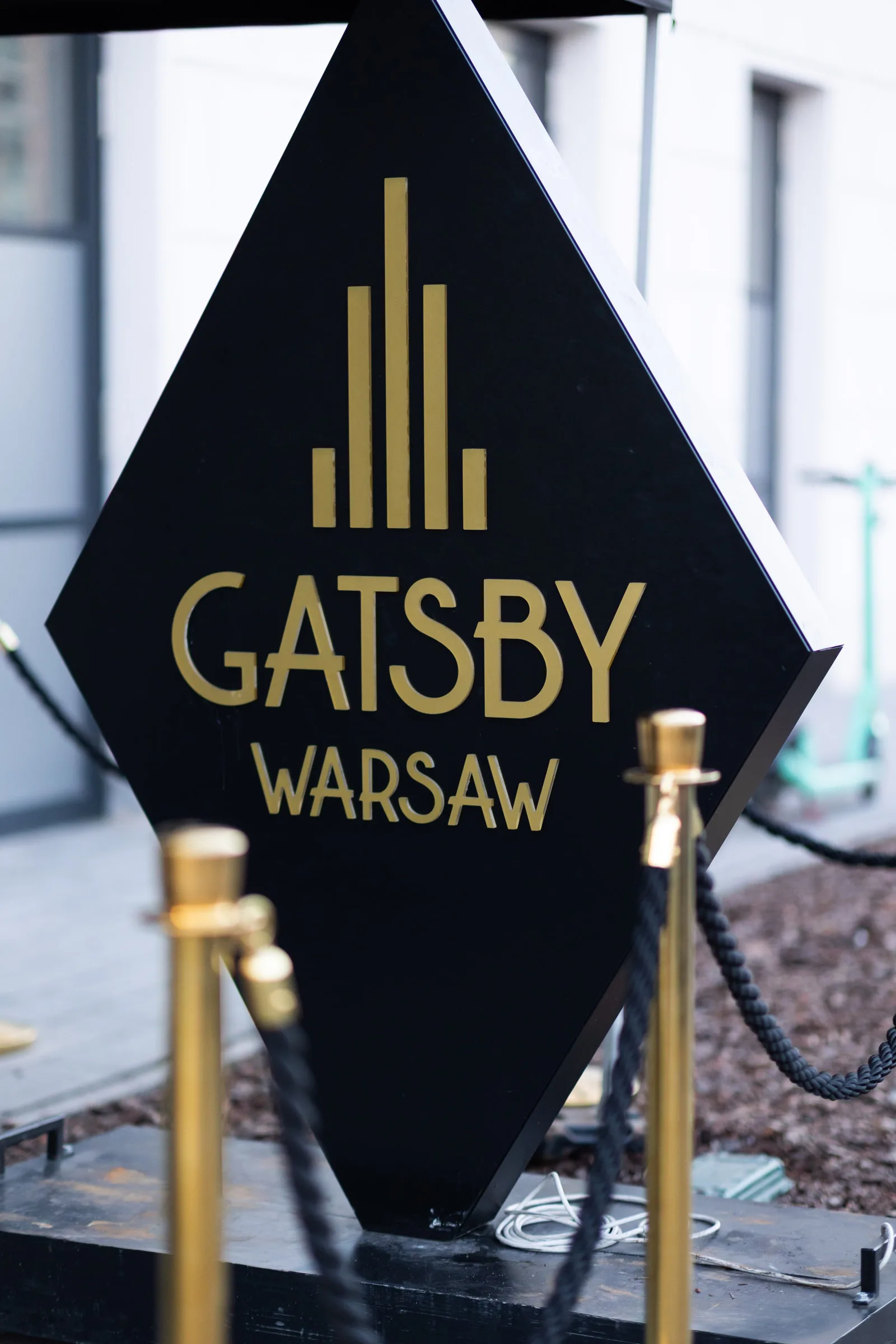 Вивіска Gatsby Warsaw із золотими стійками та канатним огородженням біля входу