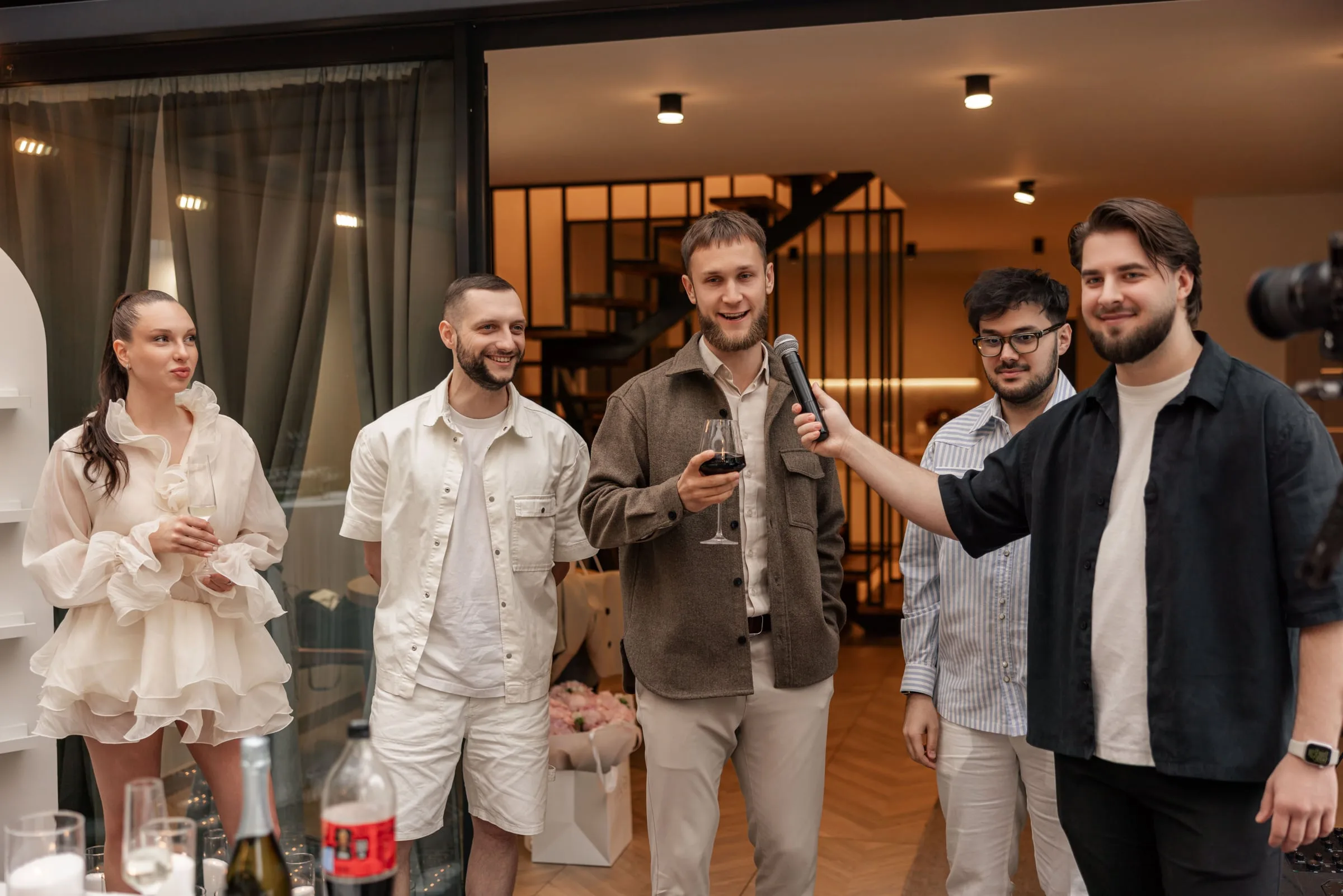 Makar holding the microphone out to a guest giving a toast with a glass of red wine