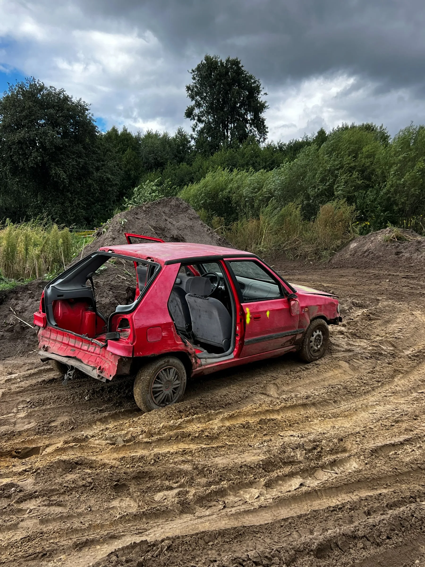 Red car missing its rear doors and bumper on a churned-up muddy track after the racing
