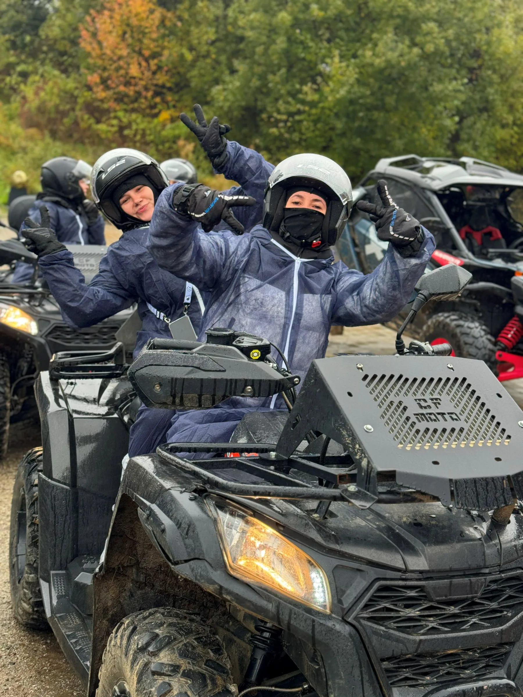 Дві учасниці в захисних комбінезонах і шоломах на квадроциклі показують знак перемоги