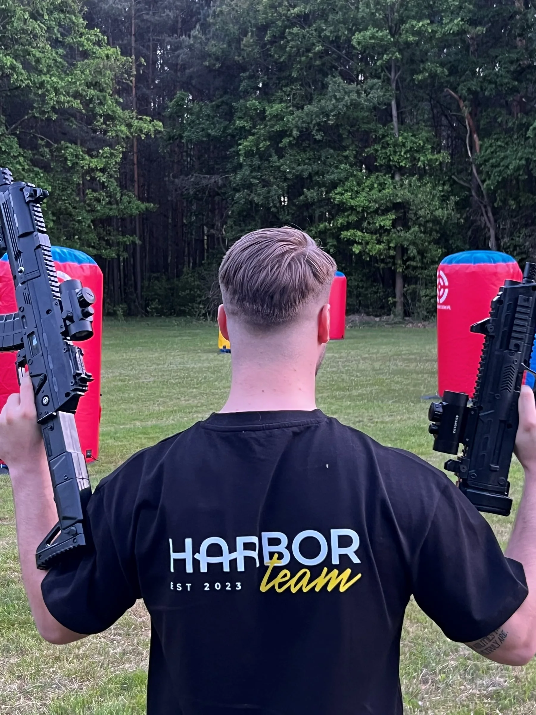 A person in a Harbor team T-shirt holding two game blasters against inflatable obstacles