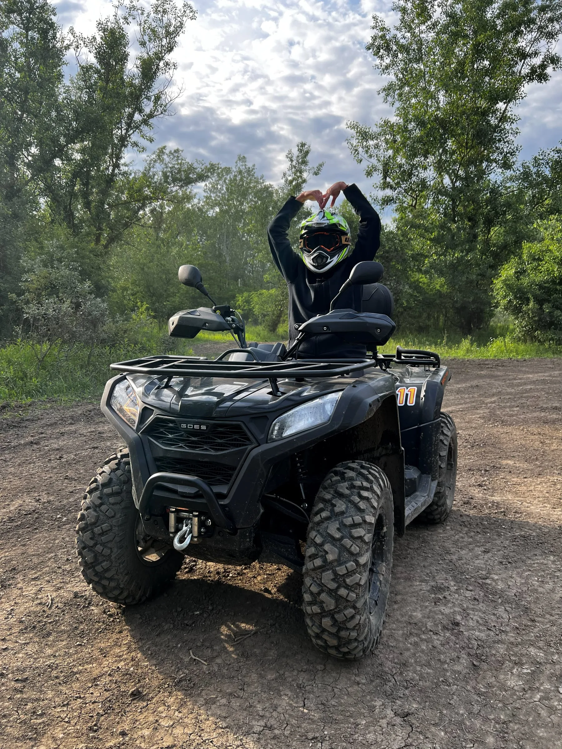 A participant in a helmet on a quad bike making a heart shape with their hands