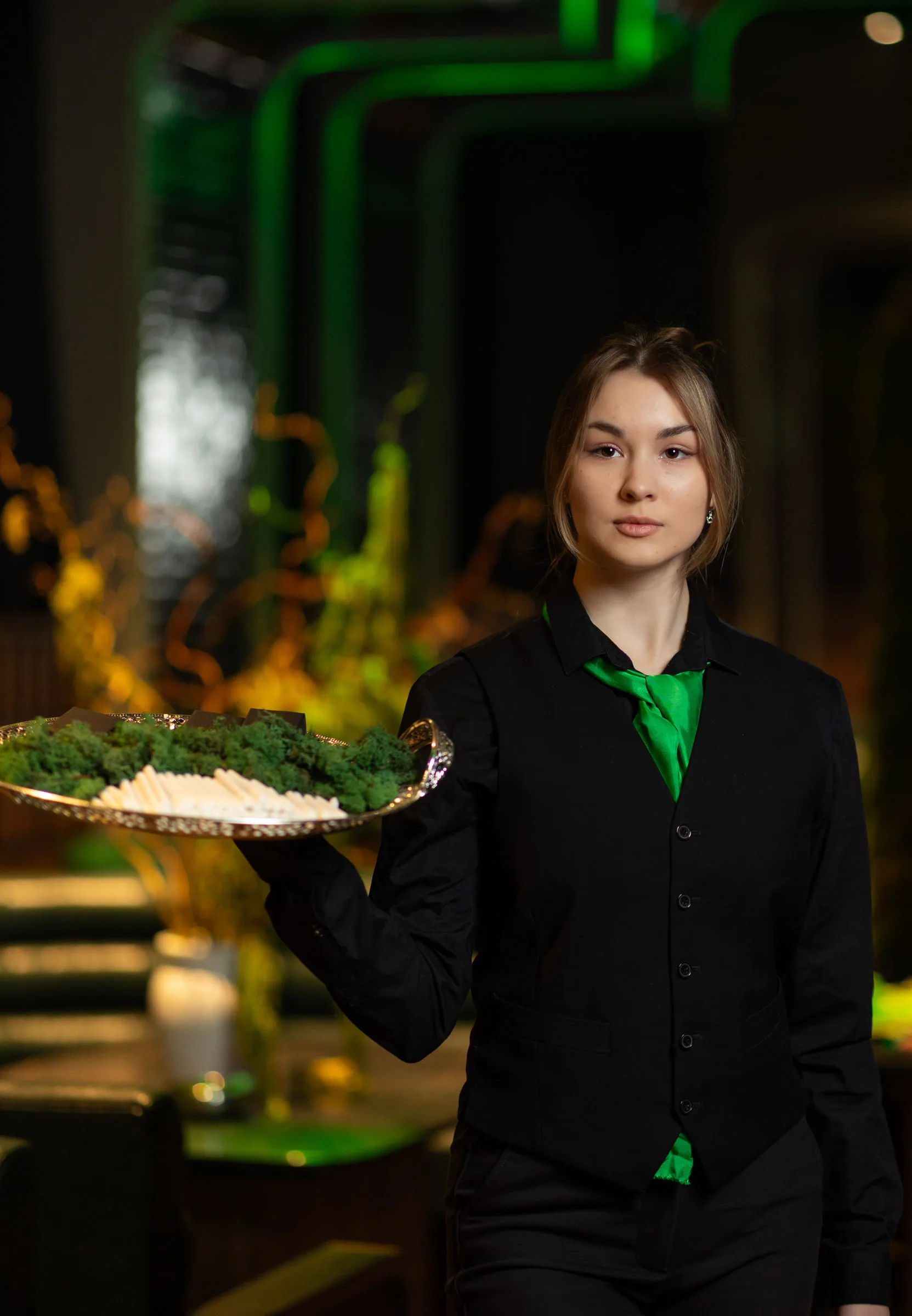 Офіціантка з тацею, викладеною мохом, на тлі зеленої підсвітки та декору з гілок